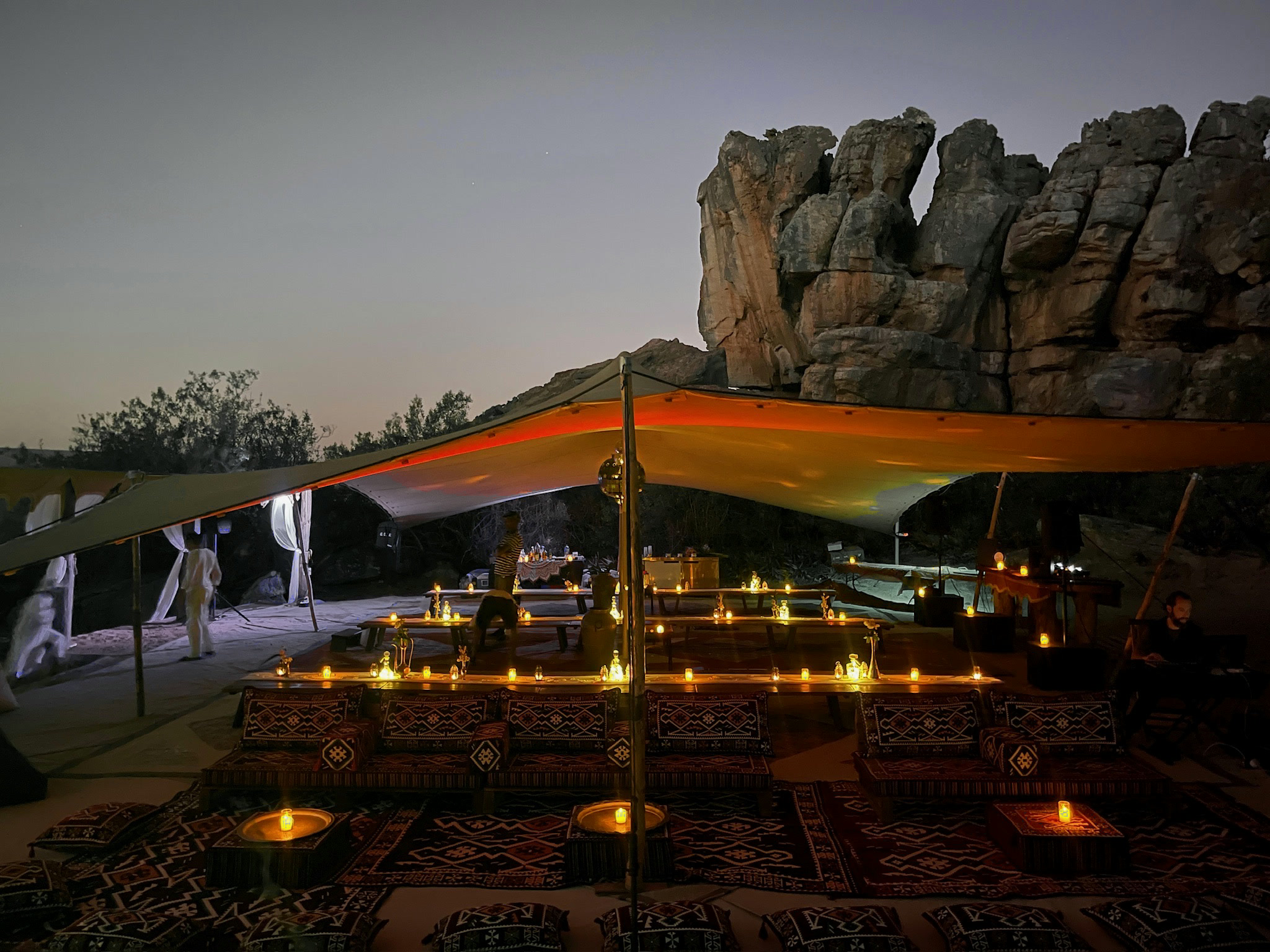 Low tables and kilim cushions under the canvas at nightfall, candles lit, the rock behind